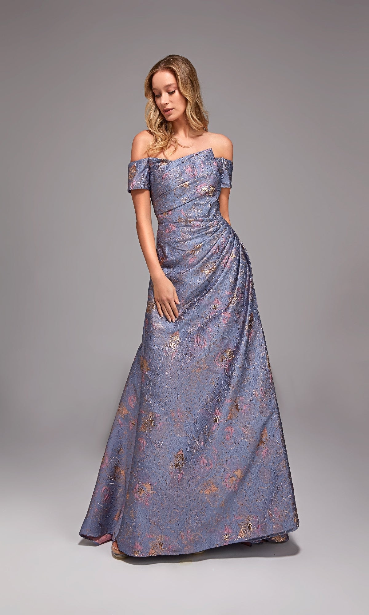 A woman stands on a plain gray background wearing the Alyce 27828, a floor-length formal dress in lilac jacquard fabric with an off-the-shoulder neckline and subtle floral pattern.
